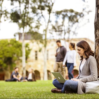 A woman sitting under a tree with a laptop.